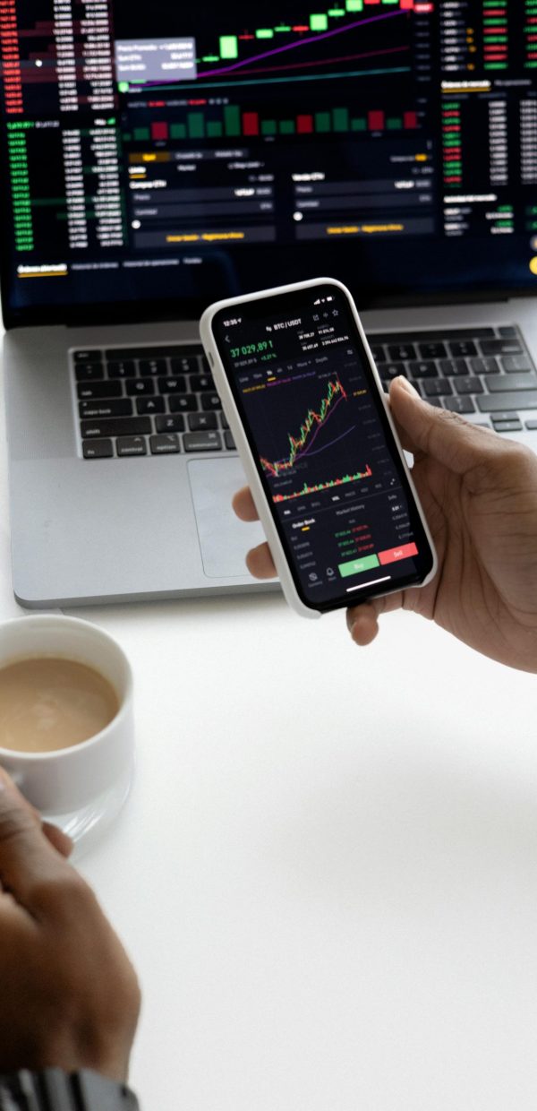 Person analyzing stock market trends on smartphone with laptop background