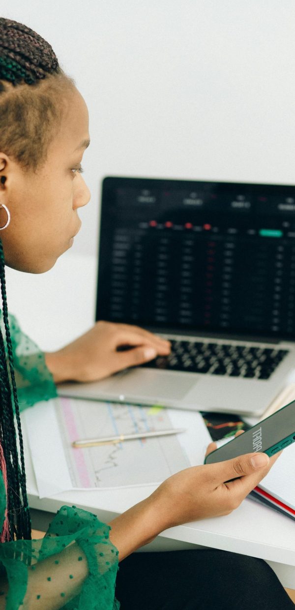 Focused woman working with financial data on laptop and smartphone in modern office.